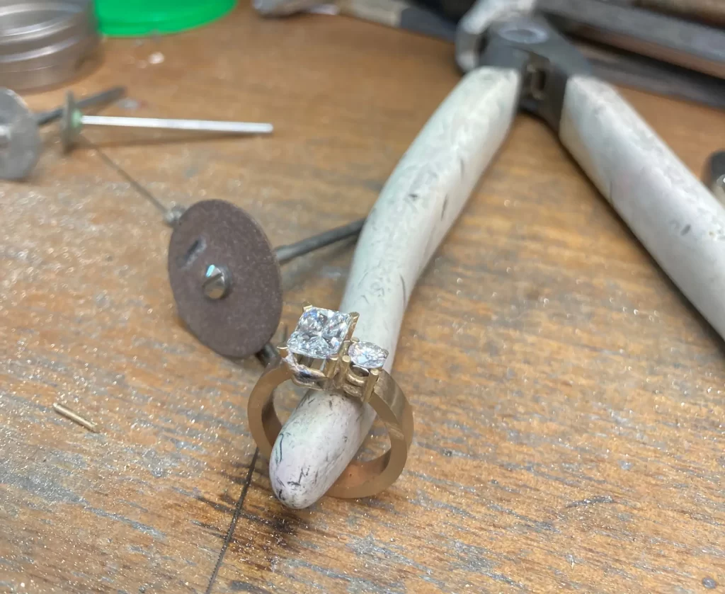 A diamond ring placed on a pair of pliers in a jeweler’s workshop, surrounded by various jewelry tools and equipment on a wooden workbench.